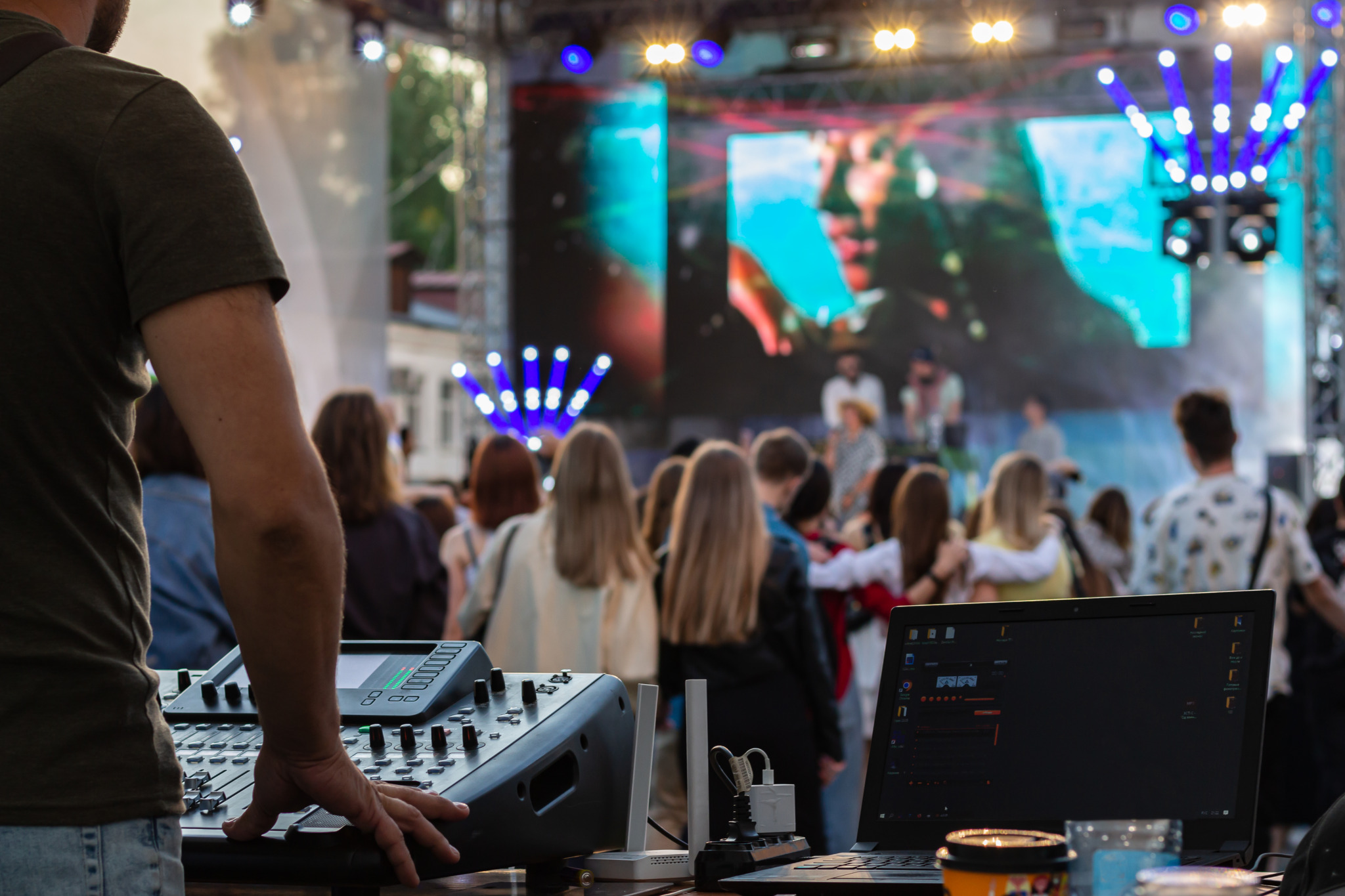 Dj mixing, laptop outdoors at party festival with crowd of people in background. Fun, summer, youth, nightlife, music and entertainment concept. low light. selective focus. professional DJ music mixer